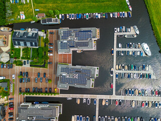 A top-down view of a marina with multiple boats docked along wooden piers, a boat cruising through...