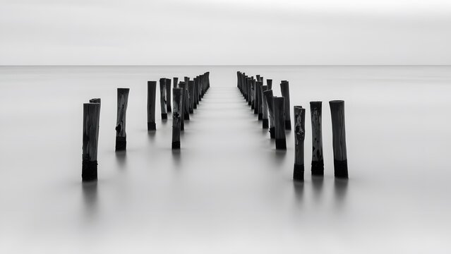 A serene black and white scene of a pier extending into calm waters, evoking tranquility and minimalism. - Powered by Adobe