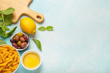 Fresh basil, olives, lemon, olive oil, fusilli pasta and wooden cutting board are creating a frame...