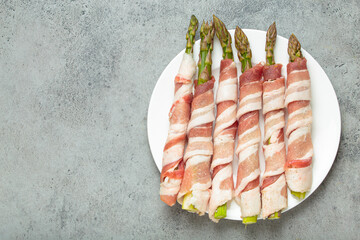 Delicious asparagus wrapped in bacon strips, seasoned with colorful peppercorns, presented on a...