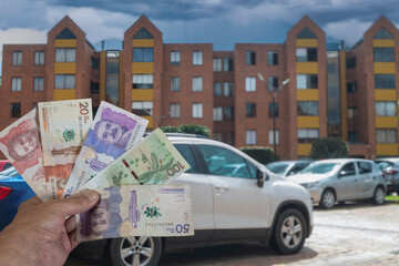 Colombian peso bills in a man's hand in front of a parking lot and apartment buildings.