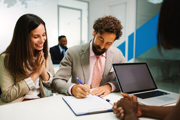 Businessman signing contract with businesswoman observing in modern office