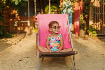 Funny cute girl on summer vacation. The child has fun near the pool. Cute baby girl in a colorful swimsuit and sunglasses is resting.