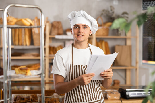 Thrilled entrepreneur in green apron reacting with excitement while reviewing financial documents showing increased profits in small artisan bakery