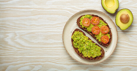 Two slices of whole rye bread are topped with mashed avocado, green peas, cherry tomatoes, and sesame seeds, a healthy and vibrant breakfast or snack option