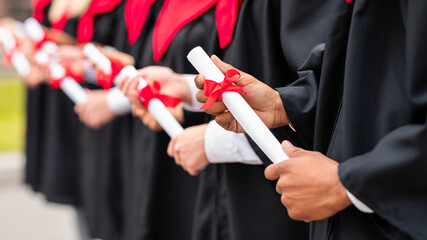 Cropped of international group of graduates in black and red graduation costumes standing in a row...