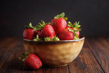 Fresh red strawberries in a rustic bowl on a dark wooden background. Front view