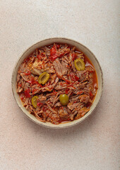 Ropa vieja, a traditional Cuban dish, is served with white rice, tomato sauce, and green olives on a plate from above on light beige background