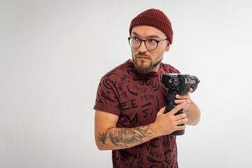 Playful young male photographer in red beanie posing with camera in hand like a superhero. Tattooed...