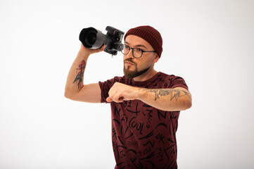 Playful young male photographer in red beanie posing with camera in hand like a superhero. Tattooed...