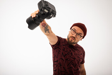 Playful young male photographer in red beanie posing with camera in hand like a superhero. Tattooed...