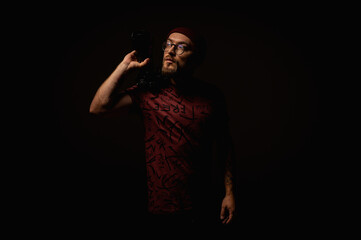 Moody portrait of a stylish photographer in beanie and glasses holding a camera on shoulder....