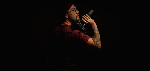 Moody portrait of a stylish photographer in beanie and glasses holding a camera on shoulder....