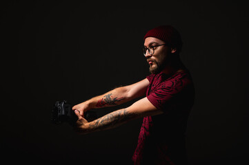 Moody portrait of a stylish photographer in beanie and glasses holding a camera on shoulder....