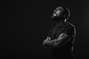 Confident man in beanie, glasses, and tattoos, arms crossed. Striking black and white studio...