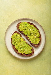 Mashed avocado seasoned with sesame seeds is spread on two slices of toasted rye bread, served on a plate over a green background, a healthy and delicious breakfast or snack