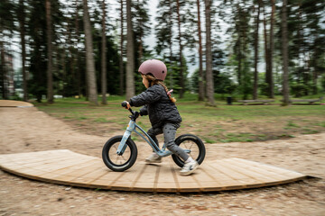 Fototapeta premium little child riding balance bike on wooden curved track in forest park, outdoor activity for toddlers, early cycling skill development, kids sport training, natural playground fun, safety helmet gear