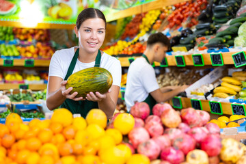 Young female seller working in a vegetable store puts melons on the counter