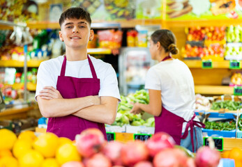 Handsome european male seller posing and offering different fresh fruit in supermarket