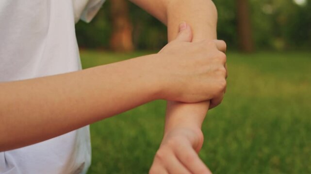 Young girl examines arm for signs of pain or irritation in sunny park environment