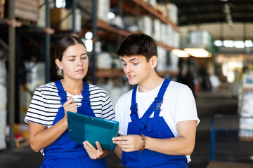 Young girl manager boss checks papers invoices together with guy employee and revise availability and quantity of goods in stock