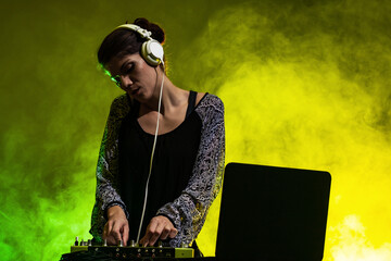 Girl DJ playing music on a mixer. Yellow and green smoke in the background