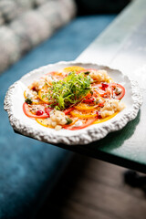 Gourmet tomato carpaccio with microgreens, diced vegetables, and sauces on a white plate, captured in a vibrant, top-down food presentation style
