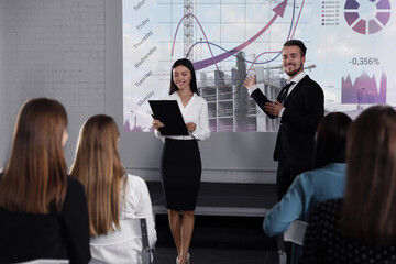 Business trainers giving lecture using video projector in conference room. Building and graphs on...