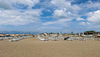 Wide Sandy Beach with Empty Sunbeds and Straw Umbrellas in Antalya, Turkey – Peaceful Seaside Scene on a Bright Cloudy Day