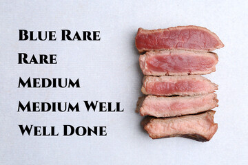Pieces of delicious beef meat in different degrees of doneness on light table, top view