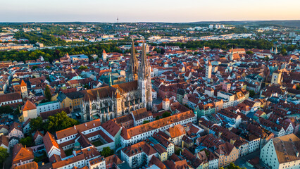 Regensburg at sunset captured from above, featuring the iconic Stone Bridge over the Danube River and the majestic twin towers of St. Peter's Cathedral glowing in warm evening light