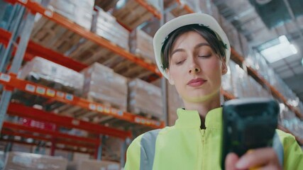 Warehouse staff member in reflective safety gear using handheld barcode scanner with red laser and holding digital tablet, conducting inventory control in aisle lined with tall racks of packed boxes.