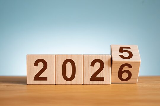 Wooden blocks display the year twenty twenty five transitioning to twenty twenty six on a wooden surface with a soft blue background