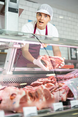Kind young male seller in work clothes holding in hands piece of meat in meat-store