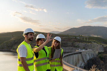 Engineers using laptop discussing project near dam at sunset