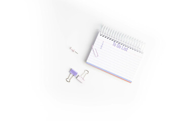 Purple To do list with 1, 2, and 3 listed on lined paper in a notebook with paper clips and push pins on white background,