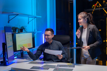 Happy smiling young Asian man and woman teammate officer have overwork project overnight in office,...