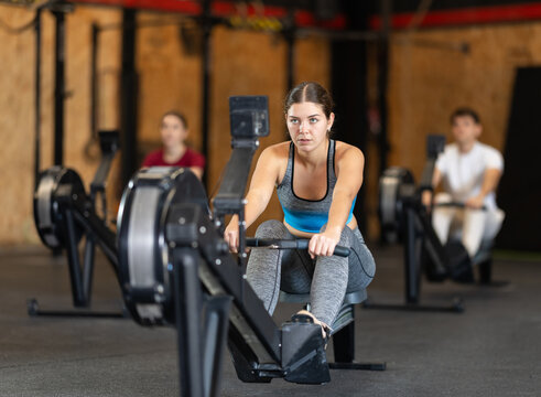 Woman performs exercises on a rowing machine, keeping the pace. Athletic woman in training doing intense exercises. Client in the gym monitors the figure and goes to training