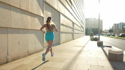 A young woman in a blue sports outfit jogs in the city, enjoying a sunny day. Concept of fitness, running, and healthy lifestyle.