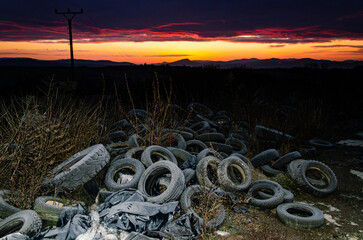 Discarded tires pollute a snowy landscape, as a vivid winter sunrise highlights environmental...