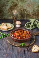 Ratatouille, vegetable stew of eggplant, zucchini, tomatoes and sweet pepper in a clay brown plate on a dark wooden background. Vegetable dishes.