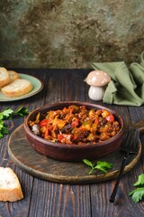 Ratatouille, vegetable stew of eggplant, zucchini, tomatoes and sweet pepper in a clay brown plate on a dark wooden background. Vegetable dishes.
