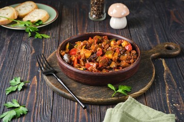 Ratatouille, vegetable stew of eggplant, zucchini, tomatoes and sweet pepper in a clay brown plate on a dark wooden background. Vegetable dishes.