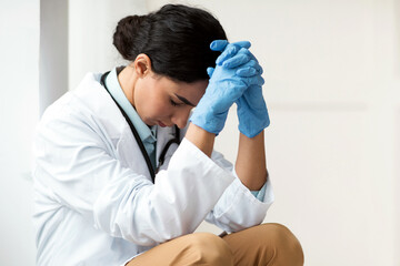 Stressed brunette young woman doctor having difficult day at clinic, wearing protective gloves,...