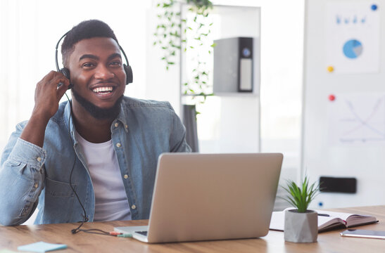 Continuing education program. Smiling african american employee in headphones watching webinar on laptop in modern office.