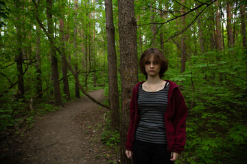 Beauty face young woman with serious thinking look hiking among green pine trees in the forest on...
