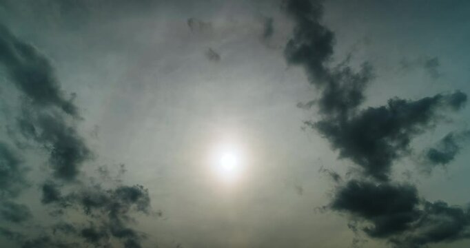 Sunlit High Veils Reveal a Bright Parhelion While Contrasting Dark Small Clouds Drift Below Creating a Layered Daytime Time Lapse of Atmospheric Optics and Moving Cloud Texture Across Translucent Sky