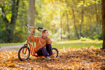 girl with orange scooter sitting on fallen autumn leaves in park, dreamy mood