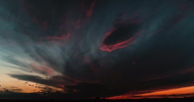 Timelapse of amazing sunset sky scene with dark clouds suddenly lightening up with bright pink color contrasting with dark grey higher clouds and accented by intense orange glow on the horizon 