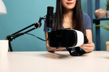 In professional studio environment, a female product reviewer demonstrates a VR headset. She...